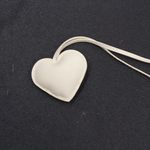 Dettaglio del ciondolo a cuore in pelle bianco crema con cuciture sottili e lacci in pelle
