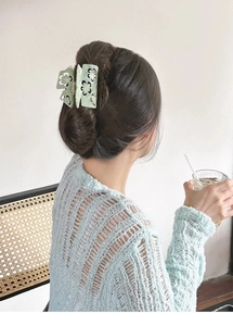 Detail of light green floral hollow hair claw clip securing a bun on a female model