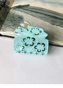 Macro detail of mint green acetate hair claw clip with hollow floral pattern and rhinestones