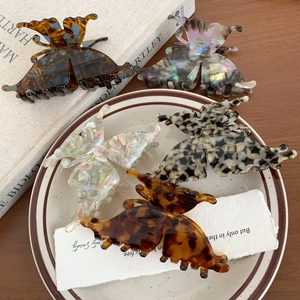 Five butterfly acetate hair claw clips with marble and tortoiseshell patterns in a ceramic dish