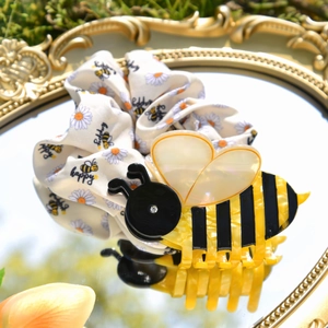 Detail of bee hair claw clip and daisy print scrunchie on a decorative mirror