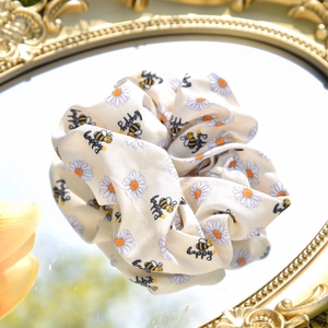 Detailed texture of beige daisy hair scrunchie with honey bee print on a mirror