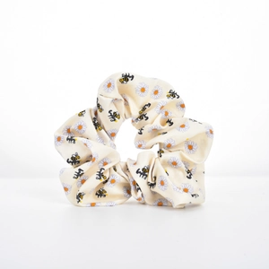 Close-up of beige satin scrunchie with daisy and happy bee print on white background
