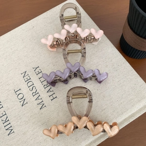 Drei elegante Haarspangen mit Herzdekor in Rosa, Violett und Beige auf einem Buch
