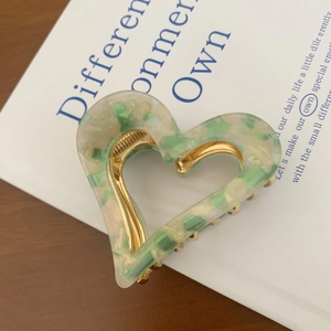 Detail of heart-shaped hair claw clip in green and white marble acetate with gold metal