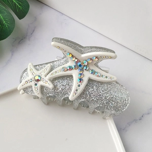 Macro shot of sparkling silver starfish hair claw clip with colorful rhinestones on marble