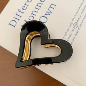 Close-up of heart-shaped hollow hair claw clip in black and gold on a vintage book