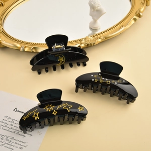 Detail of 3-piece black acetate hair claws with gold star and moon celestial patterns