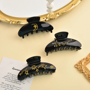 Detailed close-up of three black hair claws with celestial gold patterns and rhinestones