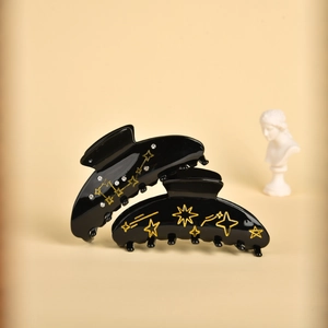 Detail of two black celestial hair claws with gold star and moon patterns and rhinestones