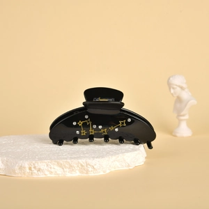Detail of black acetate hair claw clip with golden star patterns and rhinestones