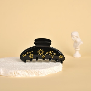 Detail view of a black acetate shark hair claw with gold star and moon patterns on a stone