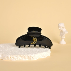 Close-up of black acetate hair claw clip featuring golden moon and star celestial patterns