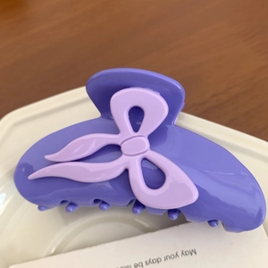 Détail d'une pince à cheveux en acétate violet avec un nœud 3D sur une surface en bois