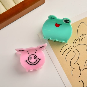Detailed close-up of cute pink pig and green frog acetate hair claws on a wooden tray