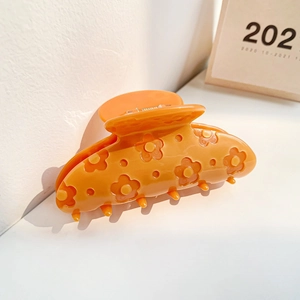 Détail d'une pince à cheveux orange en acétate avec des motifs floraux en relief