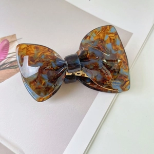 Close-up of bow hair clip with brown and blue marble pattern and gold metal inner structure