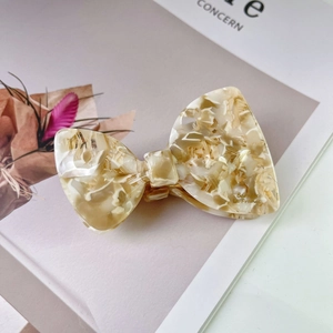 Detailed macro view of an acetate bow hair claw clip with cream marble texture on a magazine