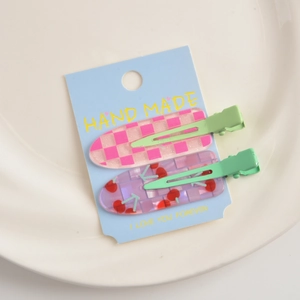 Detail of pink checkerboard and purple cherry resin hair clips on a light green metal base