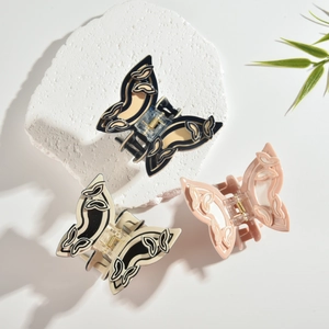 Drei Acetat-Schmetterlings-Haarklammern in Schwarz, Creme und Rosa auf weißem Stein