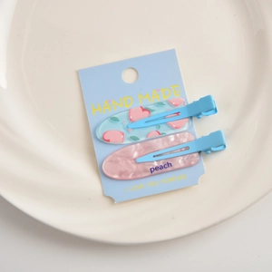 Detail shot of two peach-themed acrylic hair clips on a light blue display card
