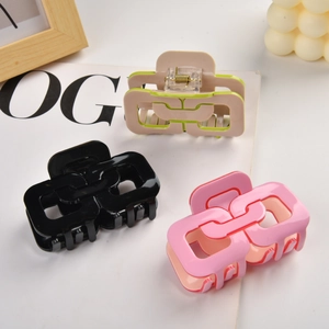 Trois pinces à cheveux géométriques en noir, rose et beige posées sur une surface blanche