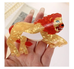 Detail view of lion-shaped hair claw clip in amber acetate with red accents and marble texture