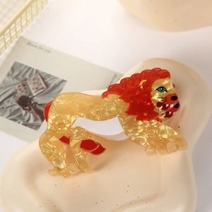 Lion shaped acetate hair claw clip with golden body and red mane on aesthetic tray