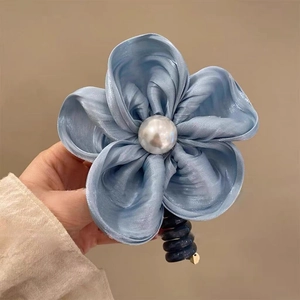 Gros plan d'un chouchou fleur en satin bleu clair avec perle et cordon spirale bleu