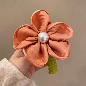 Détail d'une pince à cheveux fleur en satin avec perle et clip spirale vert