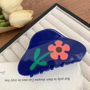 Detailaufnahme einer blauen Haarklammer mit rosa Blumenmuster auf einem beigen Tablett