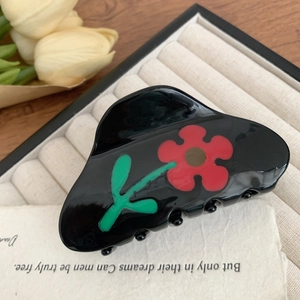 Detailansicht einer Acetat-Haarklammer mit roten Blumen auf einem beigen Tablett