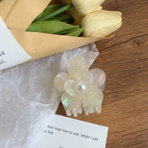 Détail d'une pince à cheveux fleur en acétate blanc nacré avec une perle centrale élégante