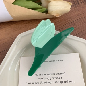 Détail de la pince à cheveux tulipe en acétate vert sur une assiette en céramique blanche