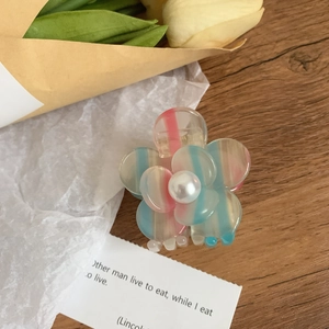 Détail d'une pince à fleurs en acétate rayé avec perle centrale sur une surface en bois