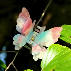 Détail de la pince à cheveux papillon dégradé rose avec paillettes dorées sur feuille