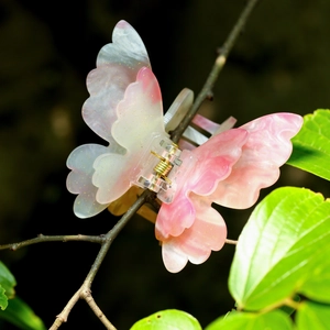Détail d'une pince à cheveux papillon en marbre rose avec paillettes dorées sur une branche