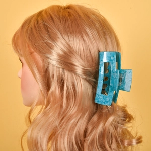 Close-up of a large blue marble acetate hair claw clip styling long wavy brown hair
