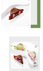 Détail de pinces à cheveux en forme de dinosaure en acétate marron, vert et rose doré