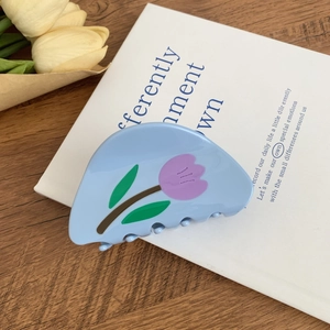 Détail d'une pince à fleurs en acétate bleu clair avec motif tulipe sur un livre blanc