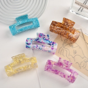 Flat lay of five large acetate hair claws with marble textures in a stylish tray
