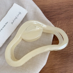 Gros plan sur une grande pince à cheveux nuage beige crème en acétate sur un tissu doux
