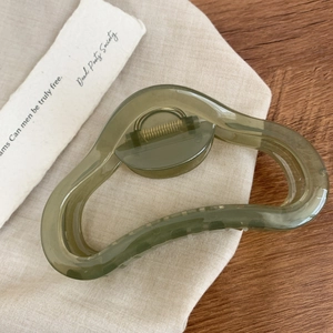 Gros plan d'une pince à cheveux vert olive translucide avec ressort doré sur tissu