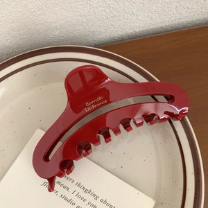 Detail of red hollow acetate hair claw clip with golden logo on ceramic plate