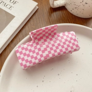 Pink checkered rectangle acetate hair claw clip on a ceramic plate for stylish hair styling