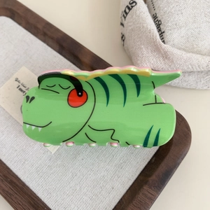 Détail d'une mignonne pince à cheveux dinosaure verte en acrylique sur un plateau