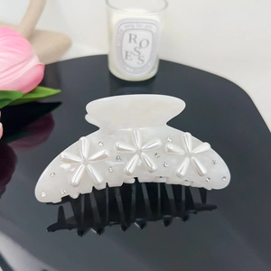 Detail of a white pearl flower hair claw with rhinestones on a reflective surface