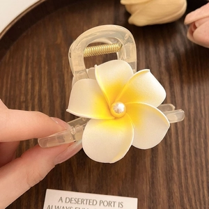 Détail d'une pince à cheveux frangipanier aux pétales blanc et jaune avec une perle centrale