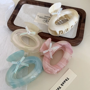 Elegant acetate oval claw clips with ribbon bows in four assorted colors on a tray