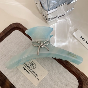Détail de la pince à cheveux en acétate marbré bleu avec nœud argenté et lettrage